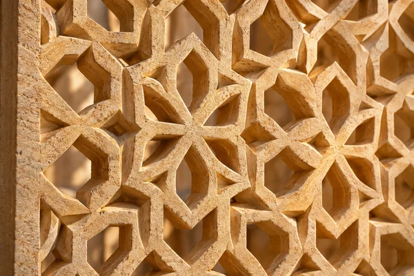 Carved warm sandstone lattice with geometric openings and soft patterned shadows.