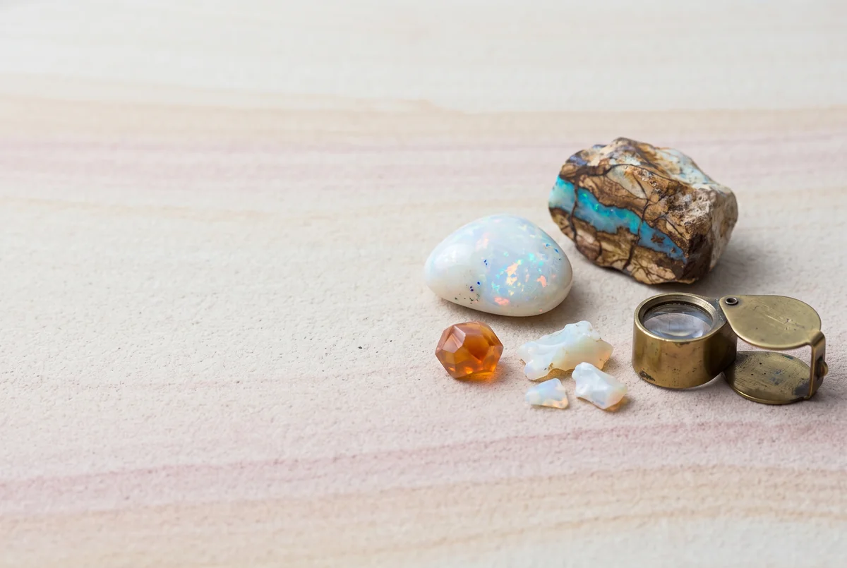 White precious opal, boulder opal and a small fire opal with a brass loupe on banded pink sandstone.