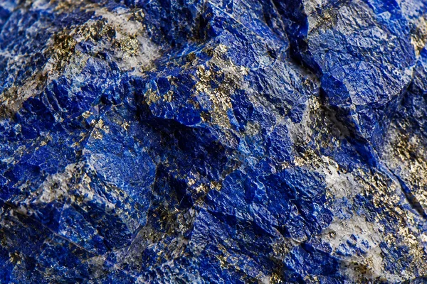 Deep blue lapis lazuli shows irregular mineral grain and small golden pyrite flecks.