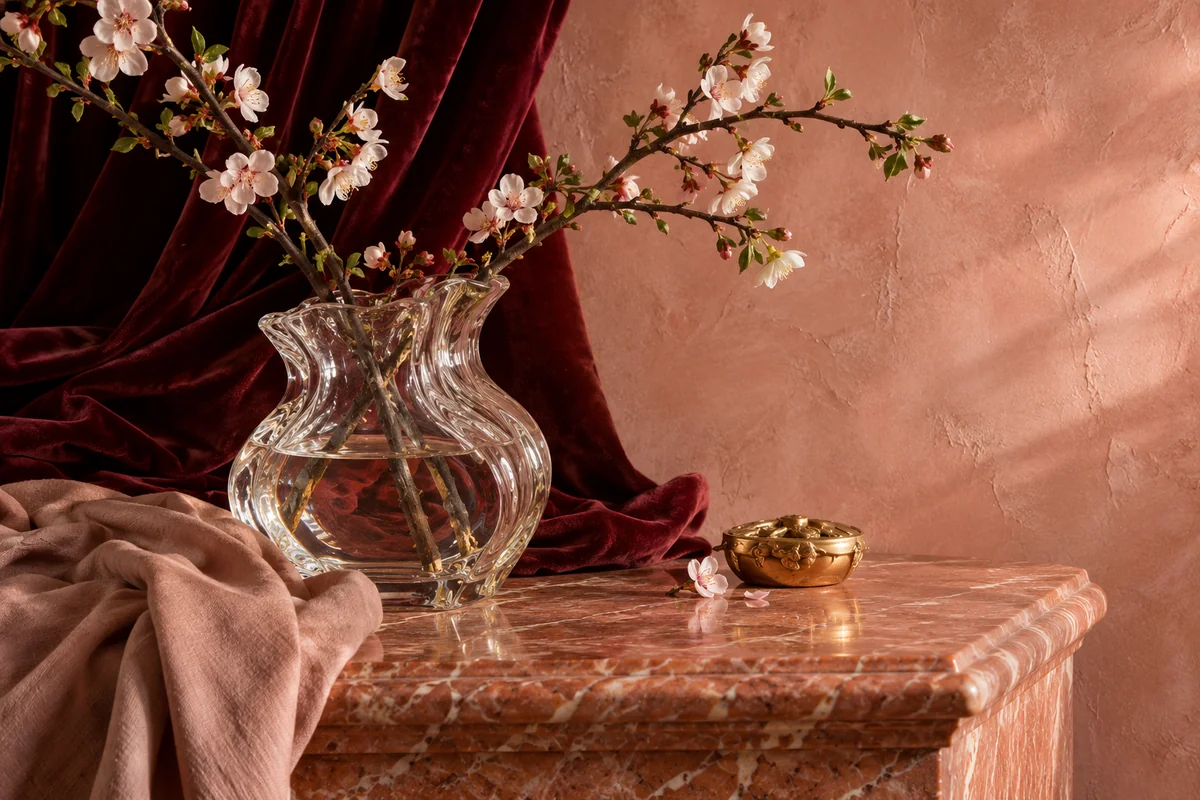 Glass vase and burgundy velvet draped beside rose marble and warm pink plaster.