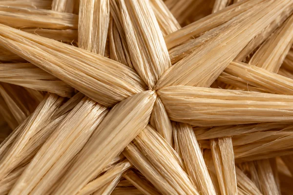 Pale golden straw woven into a star structure, showing split fibers, overlapping strands and small natural irregularities.